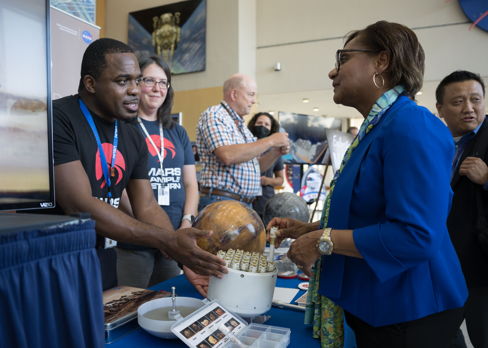 Two people discuss Mars Sample Return with a woman visiting their exhibit table.